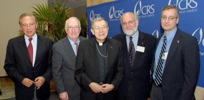 Drs. Gallo, Redfield, Amoroso stand with a bishop in front of a Catholic Relief Services banner