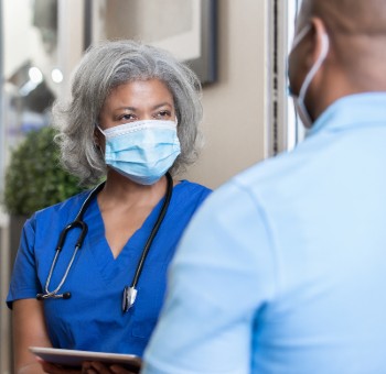 A health care provider wearing a mask talks to a masked patient